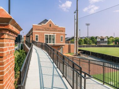 A ramp extends toward the Cantrell Family Baseball Performance Center, situated beside a baseball field under a clear sunny sky. In the background, there is a scoreboard and stadium lights.